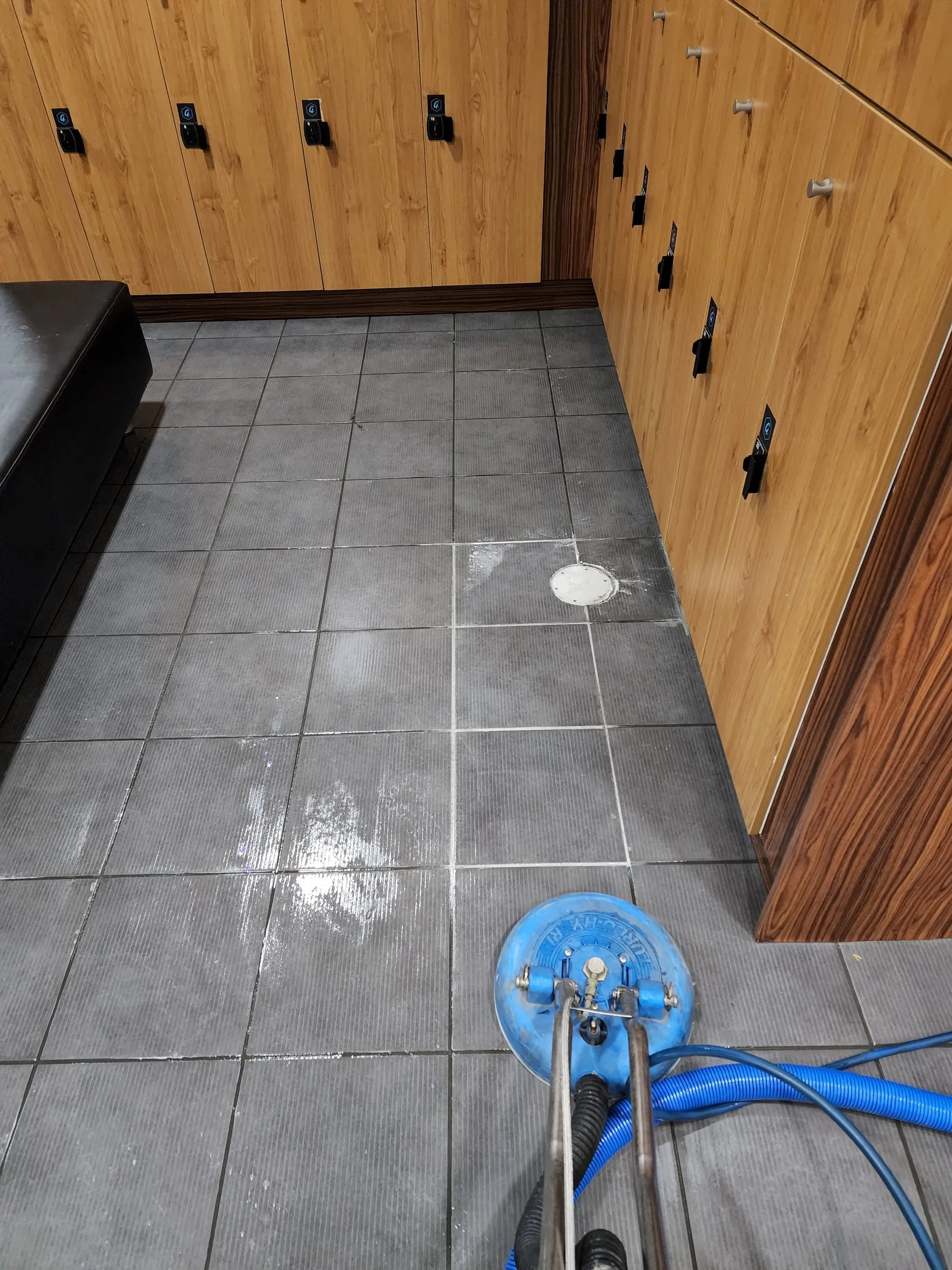 Wet change-room tiles beside lockers, with a spinner wand