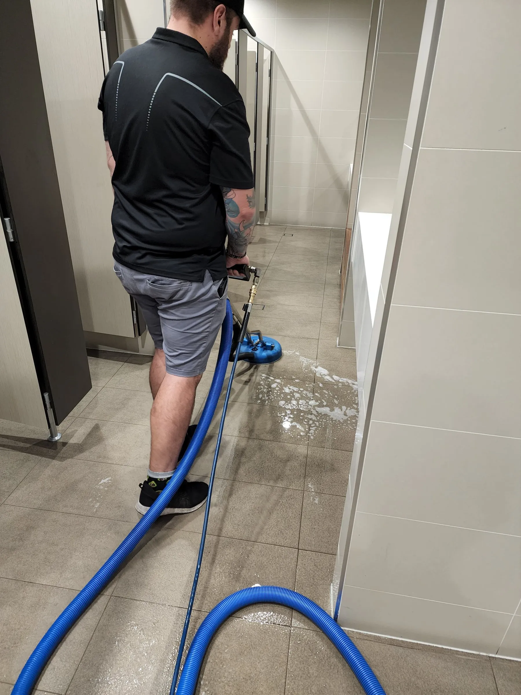Technician with a hose scrubbing a long tiled floor