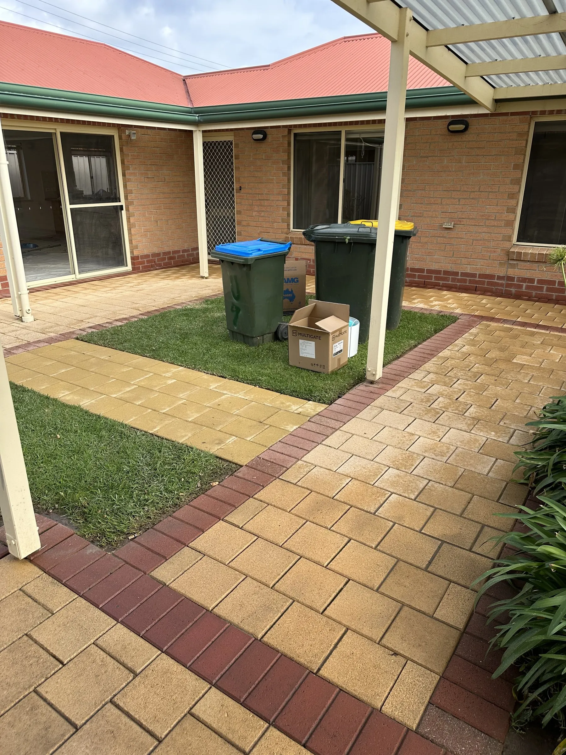 Paved unit courtyard with wheelie bins and a cardboard box beside the lawn