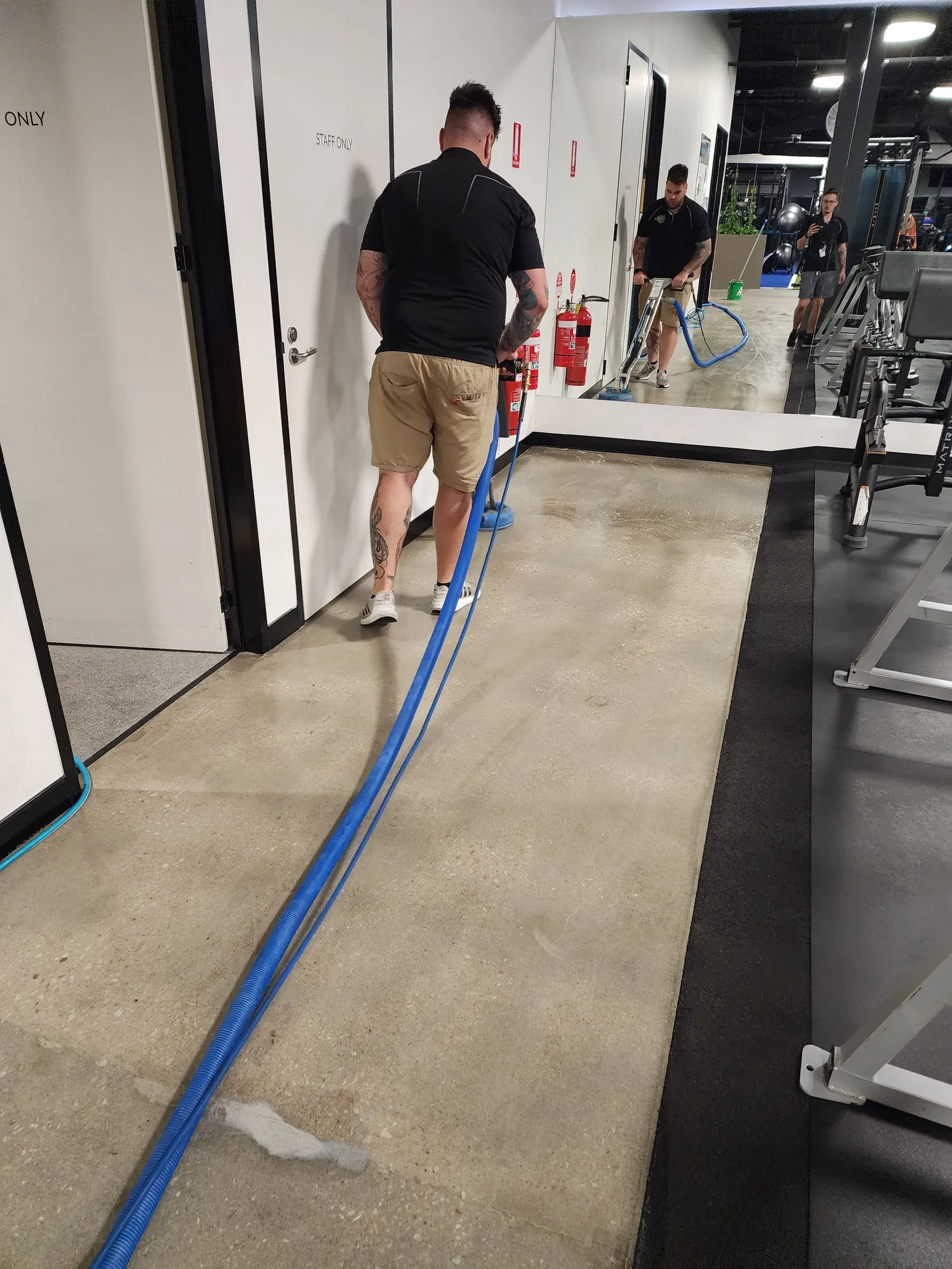 Two technicians with a hose scrubbing a polished concrete walkway inside a gym