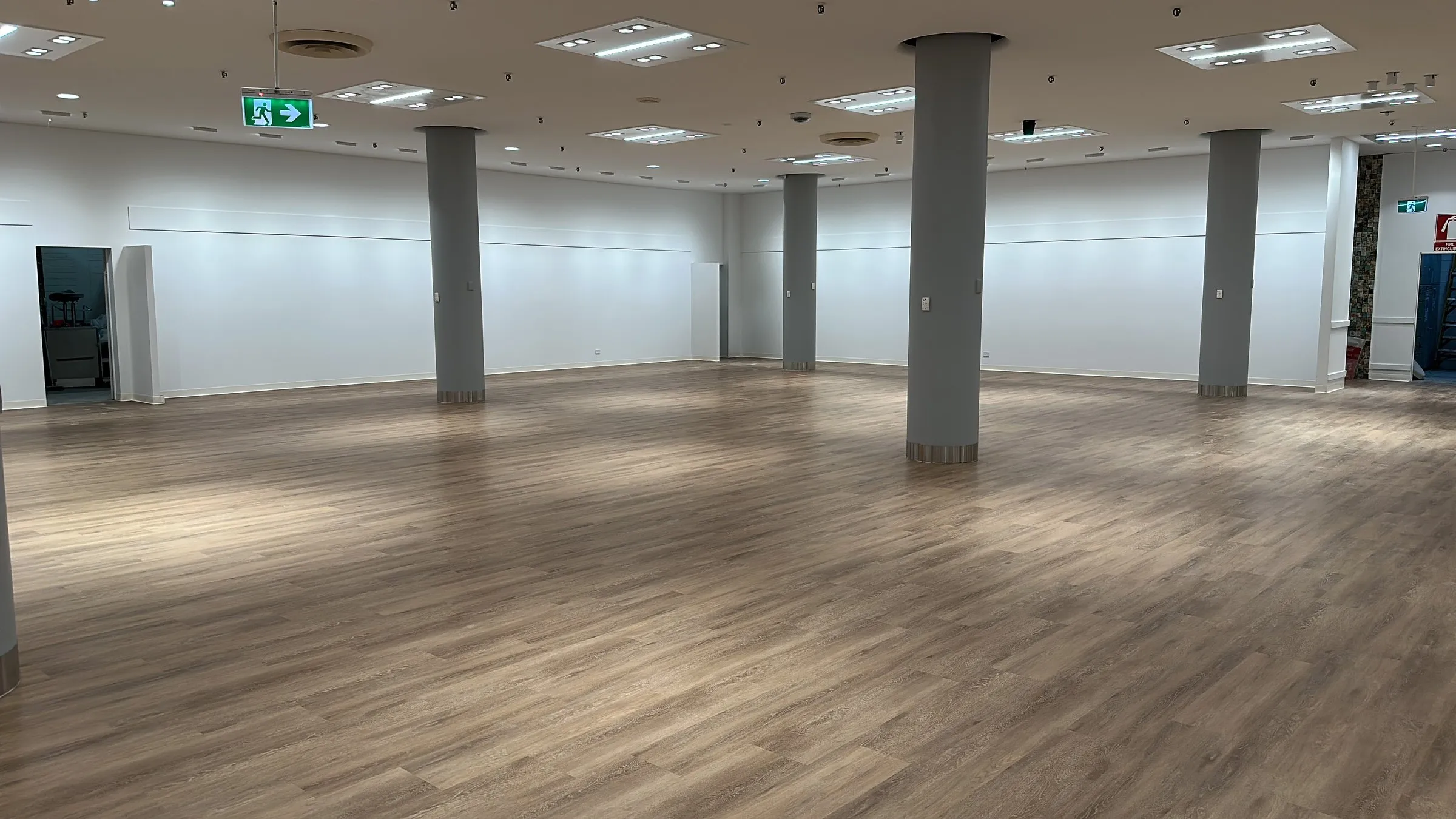 Large empty hall with a timber-look floor and grey pillars