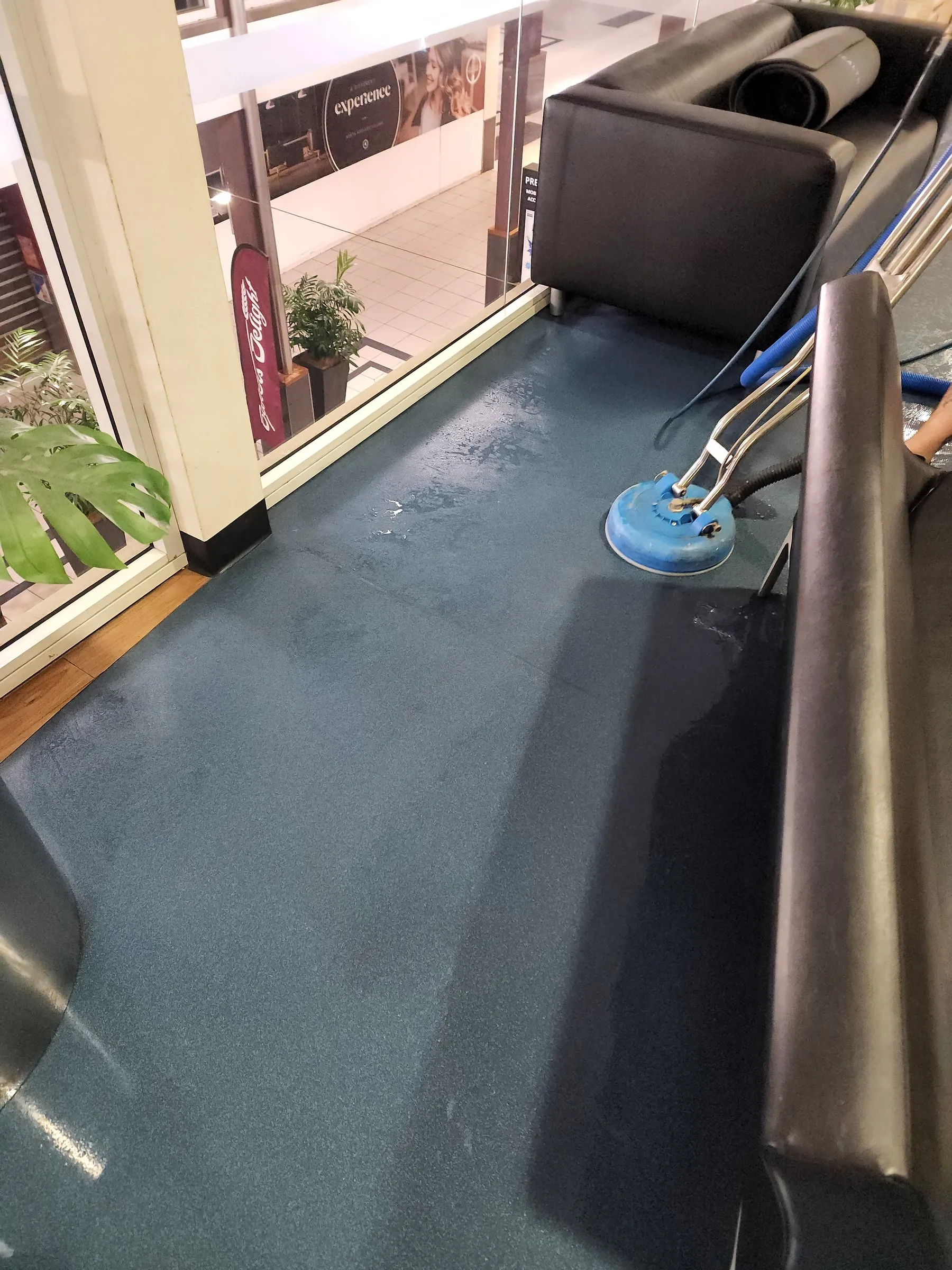 Spinner wand scrubbing a blue vinyl floor beside a lounge and a window