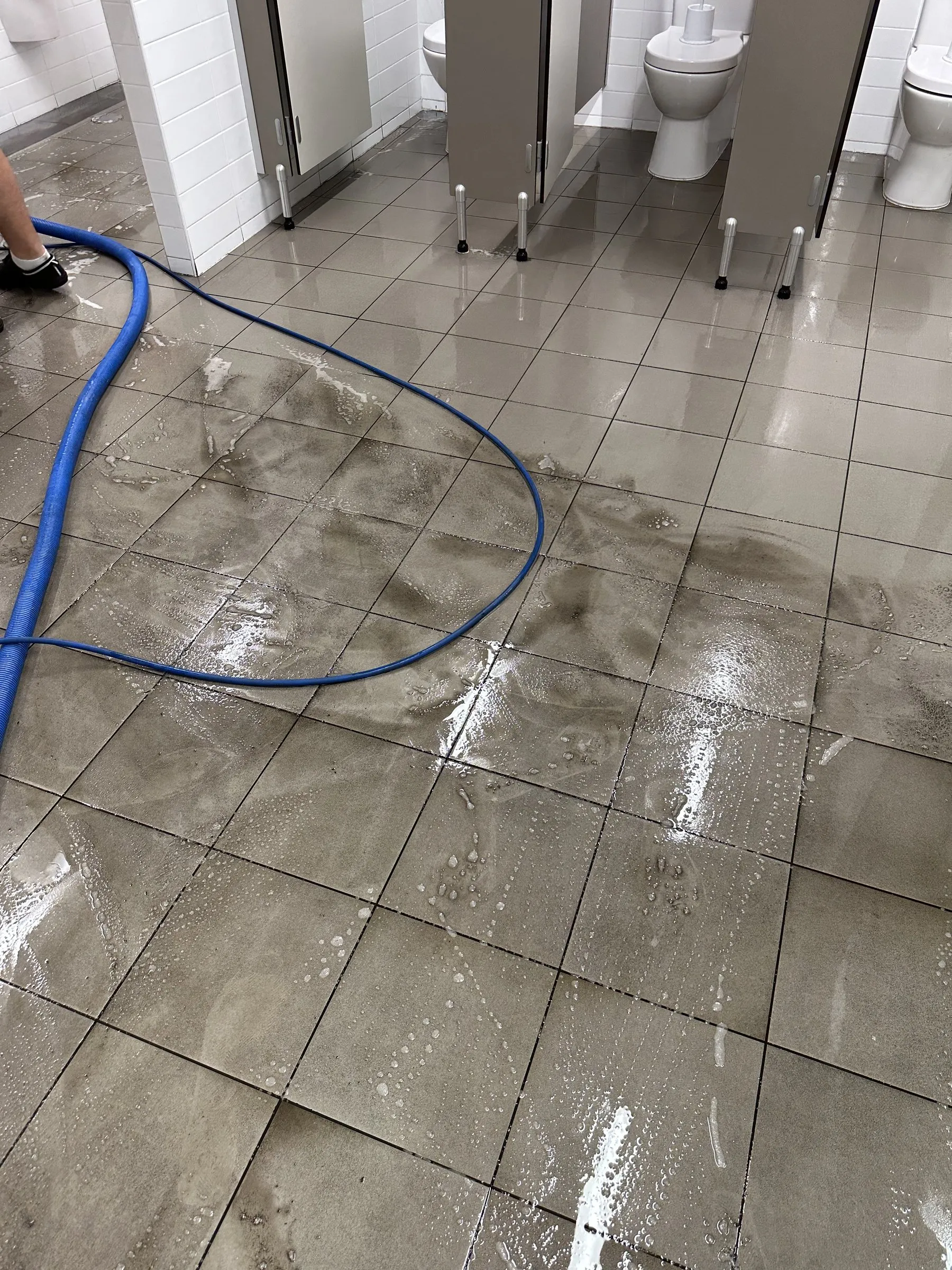 Washroom floor mid-clean with a hose, the grout still grimy